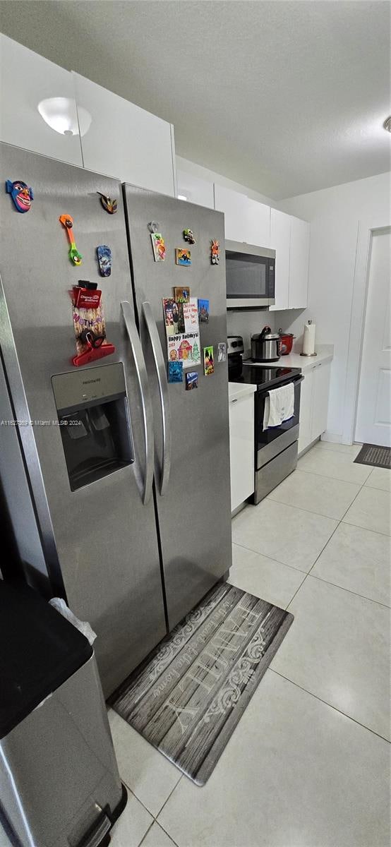 kitchen featuring appliances with stainless steel finishes, light tile patterned floors, and white cabinetry