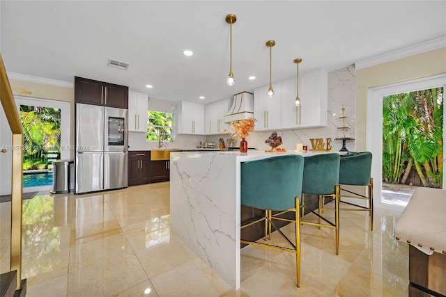 kitchen with stainless steel refrigerator, light tile patterned floors, light stone counters, and dark brown cabinetry