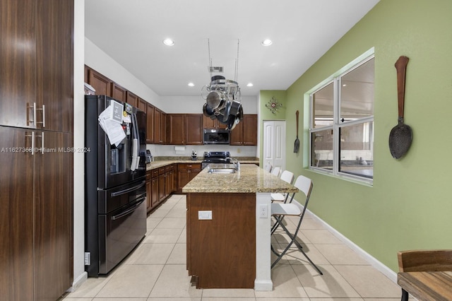 kitchen with a kitchen bar, stainless steel appliances, light tile patterned floors, a kitchen island with sink, and light stone countertops