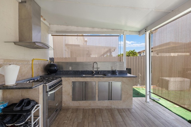 kitchen with range with two ovens, hardwood / wood-style flooring, tasteful backsplash, wall chimney exhaust hood, and sink