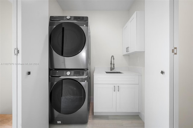 laundry room with cabinets, sink, stacked washing maching and dryer, and light hardwood / wood-style flooring