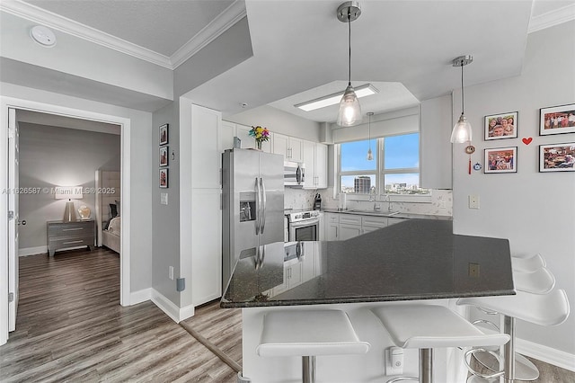 kitchen featuring stainless steel appliances, ornamental molding, white cabinetry, wood finished floors, and a peninsula