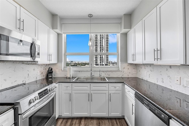 kitchen featuring dark wood-style flooring, a sink, white cabinetry, appliances with stainless steel finishes, and pendant lighting