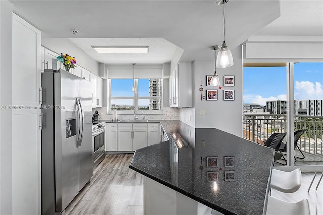 kitchen featuring light wood finished floors, appliances with stainless steel finishes, white cabinetry, a sink, and a peninsula