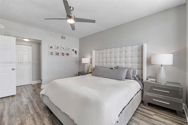 bedroom featuring a ceiling fan, a textured ceiling, visible vents, and wood finished floors