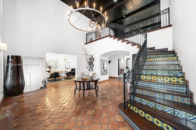 entryway featuring beam ceiling, wooden ceiling, a high ceiling, and a chandelier