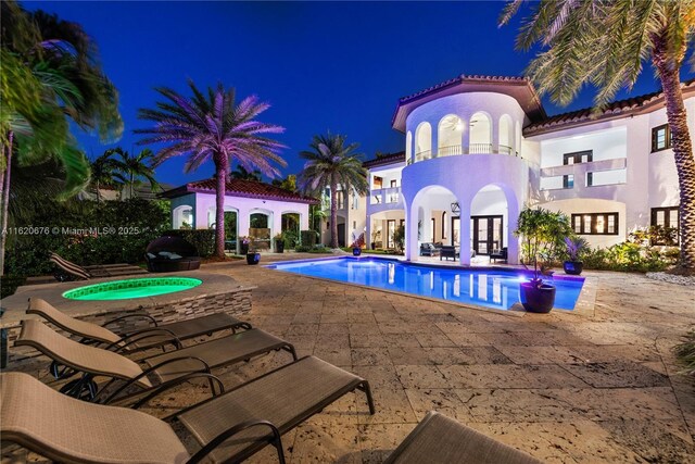 pool at twilight with an in ground hot tub and a patio