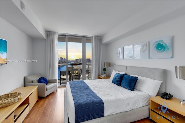 bedroom with expansive windows, a water view, wood-type flooring, and access to outside