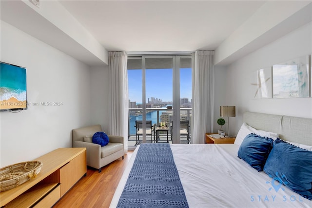 bedroom with hardwood / wood-style flooring, a water view, access to outside, and expansive windows