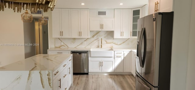 kitchen with appliances with stainless steel finishes, white cabinetry, light stone countertops, and light wood-type flooring