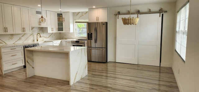 kitchen featuring tasteful backsplash, white cabinets, light wood-type flooring, a kitchen island, and appliances with stainless steel finishes