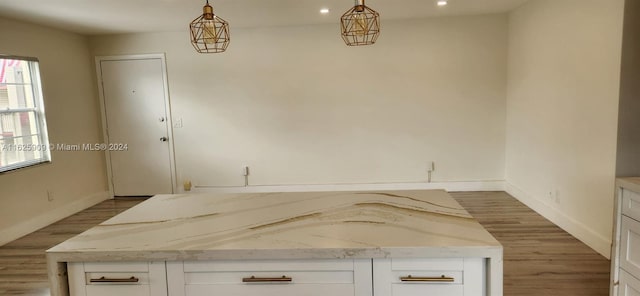 interior space featuring white cabinetry, wood-type flooring, decorative light fixtures, and light stone countertops