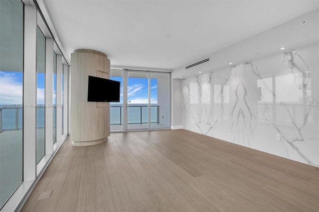 empty room featuring floor to ceiling windows, a water view, and light wood-type flooring