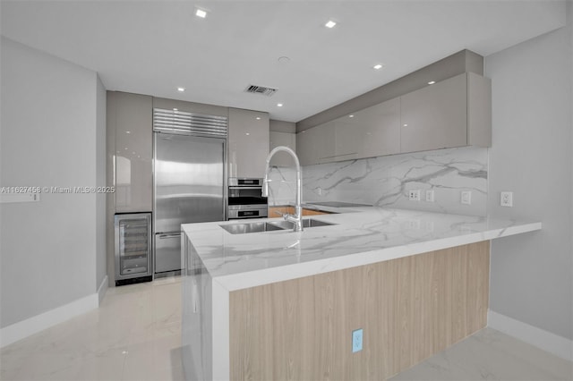 kitchen with appliances with stainless steel finishes, sink, light stone counters, kitchen peninsula, and light brown cabinets