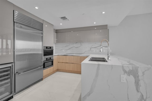 kitchen featuring sink, built in refrigerator, light stone countertops, beverage cooler, and light brown cabinets