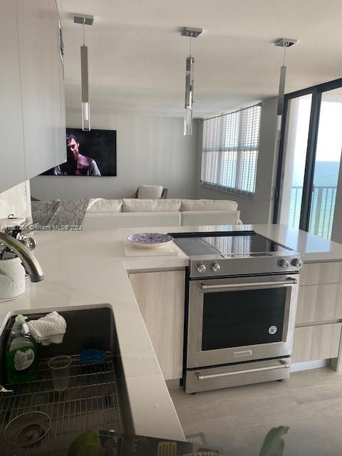 kitchen with white cabinets, sink, pendant lighting, and stainless steel range