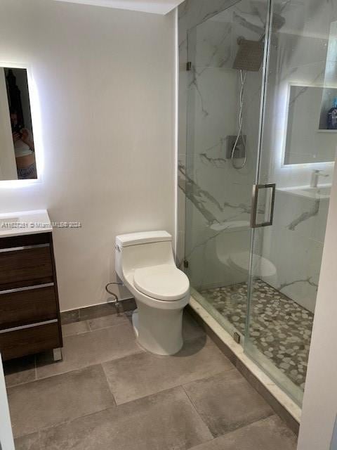 bathroom with a shower with shower door, vanity, tile patterned floors, and toilet