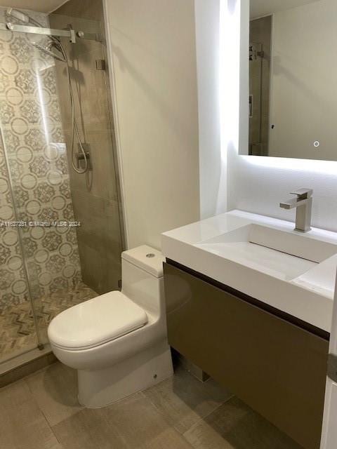 bathroom with vanity, toilet, a tile shower, and tile patterned flooring