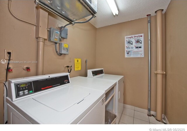 laundry area with a textured ceiling, light tile patterned floors, and washing machine and clothes dryer