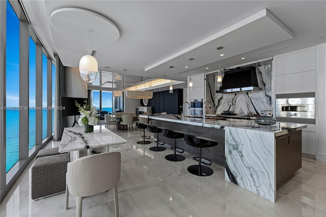 kitchen with light tile patterned flooring, light stone counters, wall oven, and an island with sink