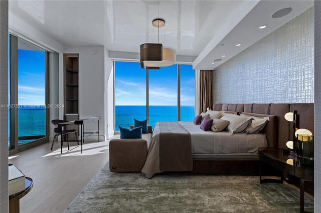 bedroom with hardwood / wood-style flooring, a water view, and multiple windows