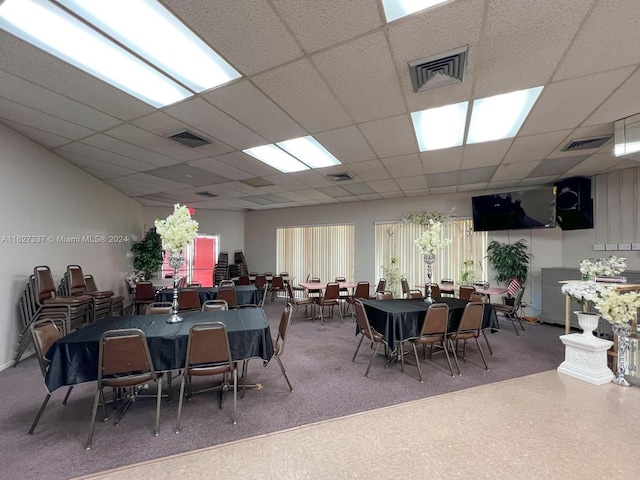 carpeted dining space with a drop ceiling