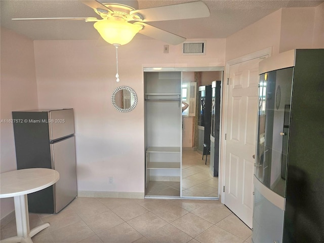 kitchen with light tile patterned floors, stainless steel fridge, ceiling fan, a textured ceiling, and black fridge