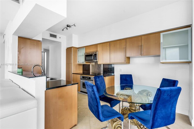 kitchen with light tile patterned flooring, sink, track lighting, kitchen peninsula, and stainless steel appliances