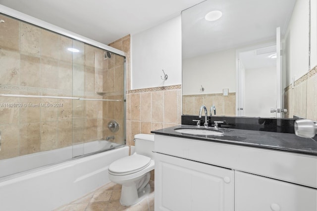 full bathroom with toilet, bath / shower combo with glass door, tile walls, and vanity