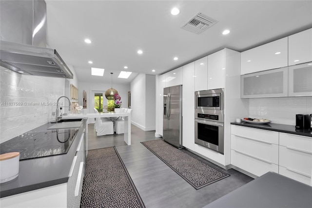 kitchen featuring wall chimney range hood, backsplash, dark hardwood / wood-style floors, stainless steel appliances, and hanging light fixtures