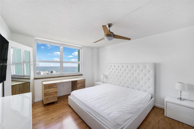 bedroom featuring ceiling fan, a water view, a textured ceiling, and hardwood / wood-style flooring