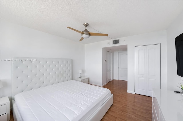 bedroom with hardwood / wood-style flooring, ceiling fan, a textured ceiling, and a closet