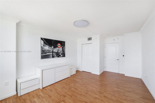 interior space with a textured ceiling, light hardwood / wood-style floors, and crown molding