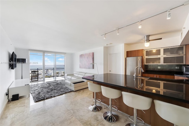 kitchen with backsplash, expansive windows, ceiling fan, stainless steel fridge, and a breakfast bar area