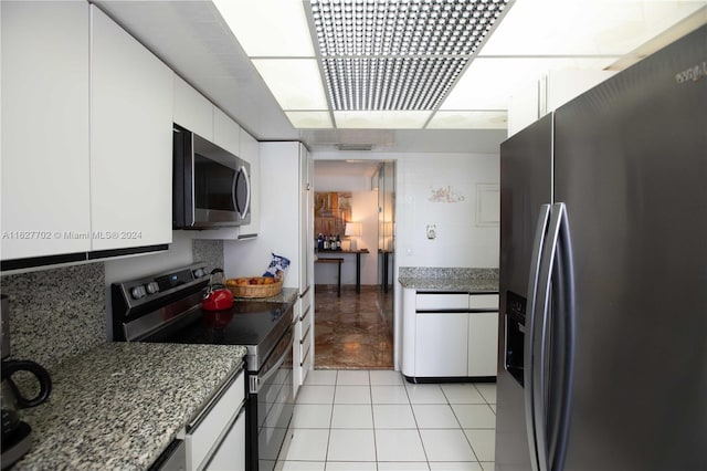 kitchen with white cabinets, light tile patterned flooring, appliances with stainless steel finishes, and stone countertops