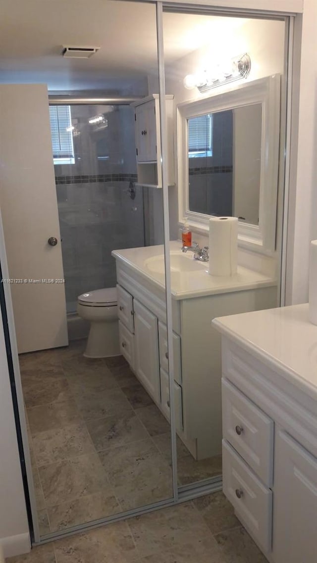 bathroom featuring a shower with door, vanity, toilet, and tile patterned floors