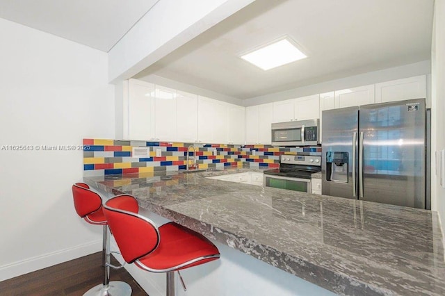 2301 Collins Ave Unit 1204, Miami Beach, FL 33139 - kitchen featuring stainless steel appliances, decorative backsplash, dark stone countertops, and white cabinets