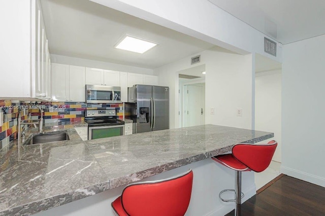 2301 Collins Ave Unit 1204, Miami Beach, FL 33139 - kitchen featuring appliances with stainless steel finishes, a peninsula, white cabinetry, a kitchen bar, and tasteful backsplash