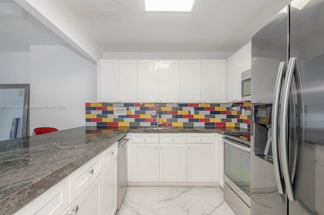 kitchen with decorative backsplash, dark stone counters, stainless steel appliances, sink, and white cabinets