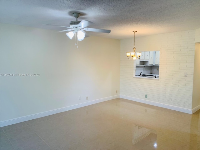 tiled spare room with brick wall, a textured ceiling, and ceiling fan with notable chandelier