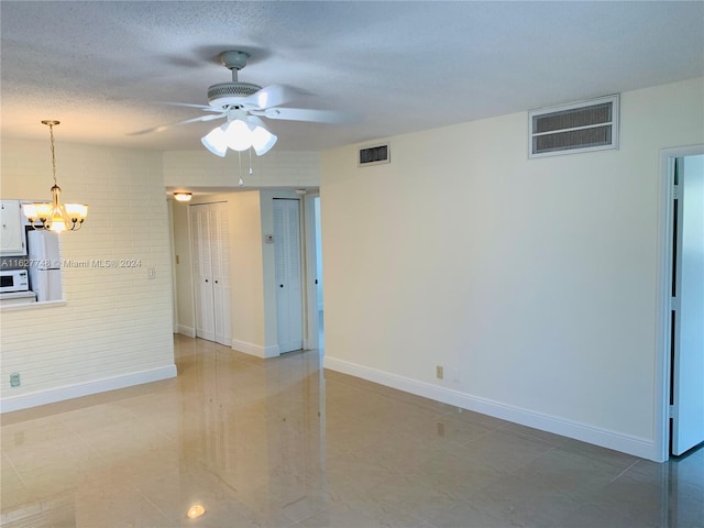 unfurnished room featuring light tile patterned flooring, ceiling fan with notable chandelier, and a textured ceiling