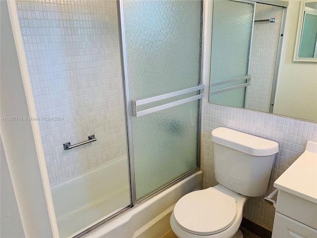 full bathroom with vanity, tile walls, bath / shower combo with glass door, and toilet