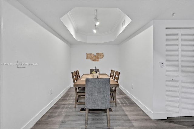 dining space with ornamental molding, wood-type flooring, and a raised ceiling