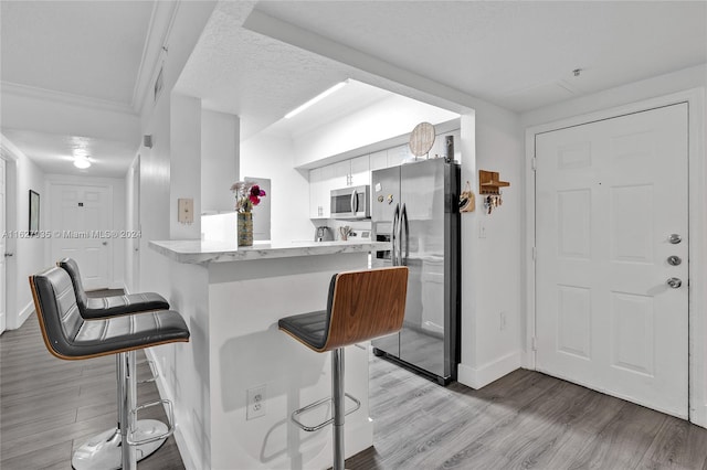 kitchen with kitchen peninsula, stainless steel appliances, white cabinetry, and a kitchen breakfast bar