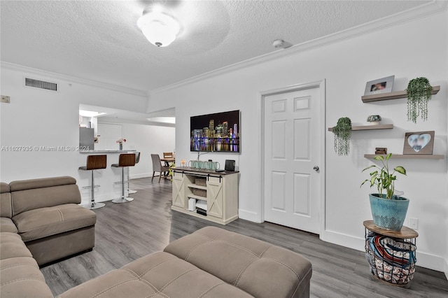 living room with indoor bar, wood-type flooring, ornamental molding, and a textured ceiling