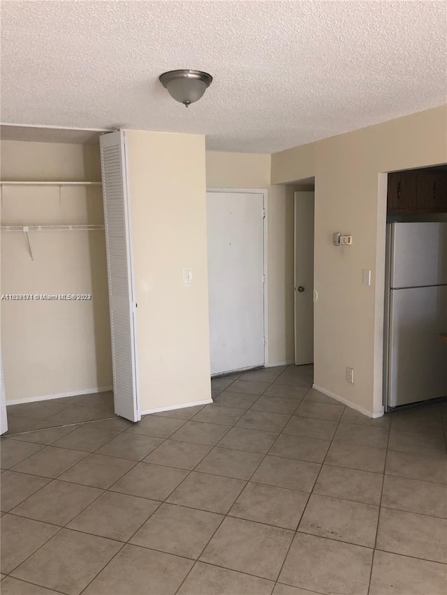 unfurnished bedroom featuring light tile patterned flooring, stainless steel fridge, a closet, and a textured ceiling