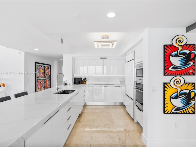 kitchen featuring sink, white cabinetry, light stone countertops, a kitchen bar, and stainless steel appliances