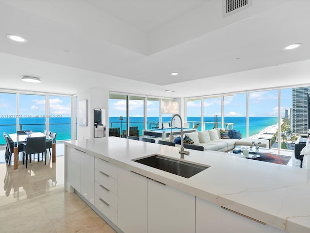 kitchen featuring white cabinetry, floor to ceiling windows, sink, a water view, and light stone counters