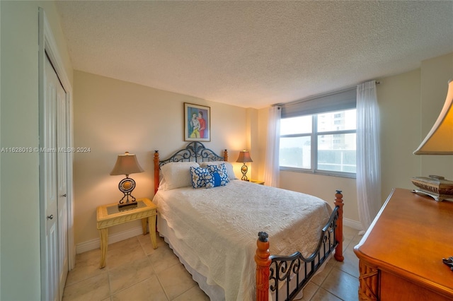 bedroom with a closet, light tile patterned flooring, a textured ceiling, and baseboards