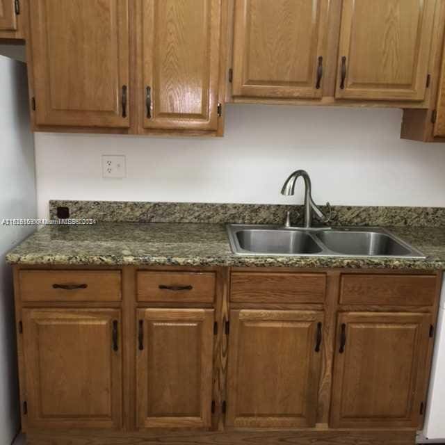 12500 NE 15th Ave Unit 207, North Miami, FL 33161 - kitchen with brown cabinetry, dark stone countertops, freestanding refrigerator, and a sink